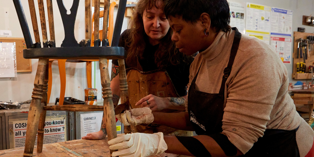 A trainee at Petit Miracles receiving guidance on furniture painting techniques, showcasing hands-on learning and creative upcycling in action