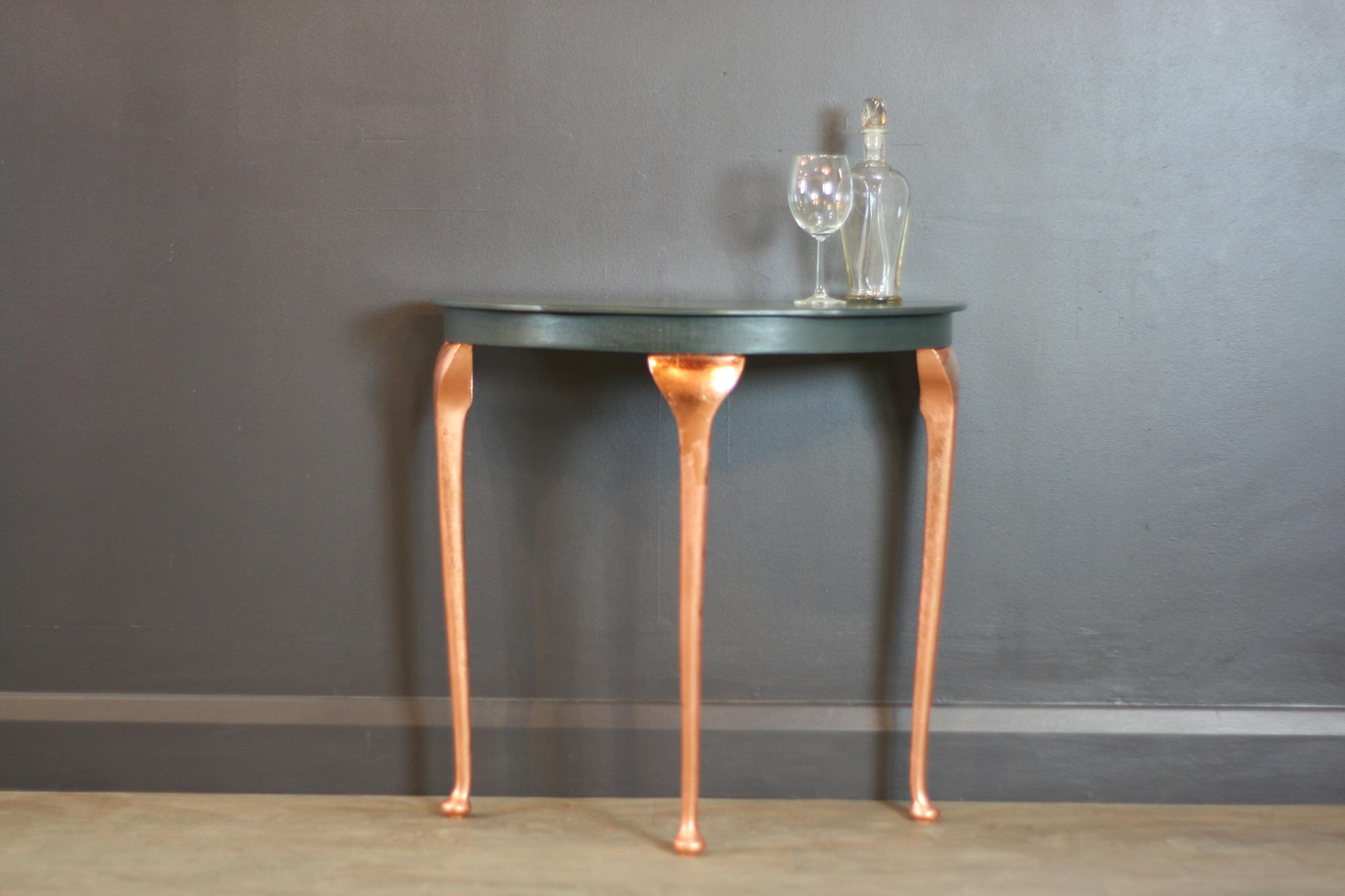 This elegant upcycled half circle console table has been meticulously hand-painted in a deep and sophisticated ‘Lamp Black’ finish, creating a sleek and timeless look. The legs have been enhanced with a luxurious rose gold metallic leaf, adding a touch of glamour and contrast to its refined silhouette. Perfect for hallways, living rooms, or dining spaces, this unique table seamlessly blends modern and vintage aesthetics, making it a statement piece for any interior. Its durable craftsmanship and eco-friendly transformation provide a sustainable and stylish alternative to mass-produced furniture.